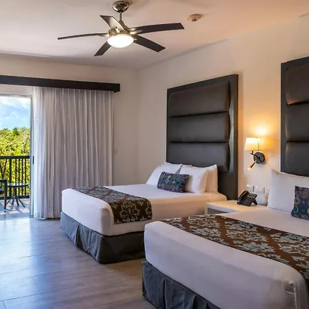 The Fives Beach Hotel & Residences - All Senses Inclusive Playa del Carmen Exterior photo The photo shows a bright and airy hotel room with two double beds. The room has white walls and light-colored wood floors. 

The beds are neatly made with white linens and decorative bed runners featuring a brown and green floral pattern. Each bed ha