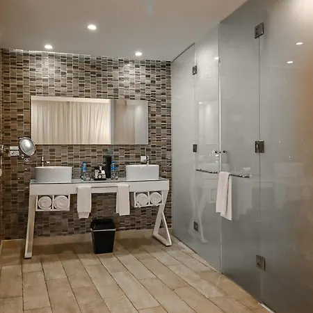 The Fives Beach Hotel & Residences - All Senses Inclusive Playa del Carmen Exterior photo The photo shows a modern and clean bathroom. The walls are covered in small, rectangular, brown and beige tiles arranged in a brick pattern, with a large mirror spanning the width above a double sink vanity. The vanity is white with two white rectang