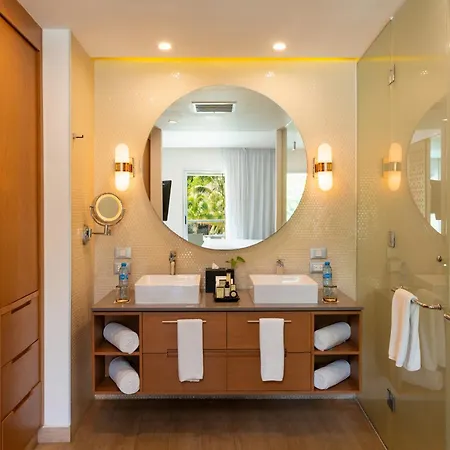 The Fives Beach Hotel & Residences - All Senses Inclusive Playa del Carmen Exterior photo This is a bright and modern bathroom with a focus on clean lines and warm tones. The main feature is a large, round mirror mounted above a wooden vanity. The vanity has two white rectangular sinks and wooden cabinets below, providing ample storage. O