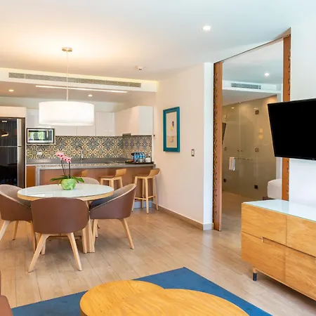 The Fives Beach Hotel & Residences - All Senses Inclusive Playa del Carmen Exterior photo The photo shows a brightly lit, modern apartment living space. The room features an open floor plan combining a living area, dining area, and kitchen. 

In the foreground, a light wooden coffee table sits on a blue rug. A portion of a brown leather s