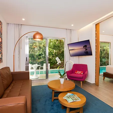 The Fives Beach Hotel & Residences - All Senses Inclusive Playa del Carmen Exterior photo The photo shows a modern and inviting hotel room with a comfortable living area and a glimpse into a bedroom. 

In the living area, a brown leather sofa sits against a white wall, adorned with a vibrant, patterned artwork. A tall, arched floor lamp w