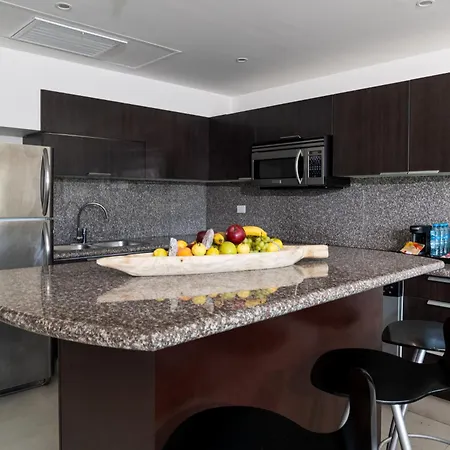 The Fives Beach Hotel & Residences - All Senses Inclusive Playa del Carmen Exterior photo The photo shows a modern kitchen with a focus on a spacious island. The kitchen features dark brown wooden cabinets above and below the countertop, which has a speckled gray granite finish. A stainless steel refrigerator stands to the left of the kit