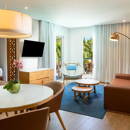 The Fives Beach Hotel & Residences - All Senses Inclusive Playa del Carmen Exterior photo The photo shows a modern and inviting hotel suite with a warm and airy atmosphere. The room is well-lit, likely by both natural light coming through large windows and artificial lighting.

The main living area features a comfortable brown sofa with s