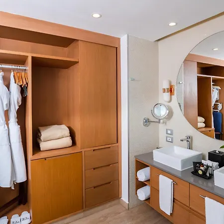 The Fives Beach Hotel & Residences - All Senses Inclusive Playa del Carmen Exterior photo The photo shows a well-lit and organized bathroom, likely in a hotel or upscale residence. The color palette is warm and neutral, dominated by light wood tones, beige walls, and a gray countertop. 

On the left side of the image, there's a large, bui