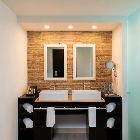 The Fives Beach Hotel & Residences - All Senses Inclusive Playa del Carmen Room photo This is a photo of a modern and stylish bathroom vanity area.

**Here's a detailed description:**

*   **Vanity:** The centerpiece is a dark, sleek vanity cabinet, likely black, with open shelving below. This cabinet supports two white, rectangular v