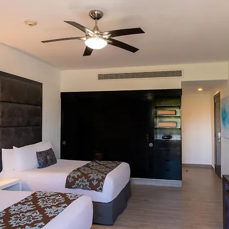 The Fives Beach Hotel & Residences - All Senses Inclusive Playa del Carmen Room photo This is an image of a modern, well-lit hotel room or guest suite.

**Key features of the room include:**

*   **Bedding:** There are at least two large beds visible, both neatly made with white linens and decorative runners featuring a dark brown and